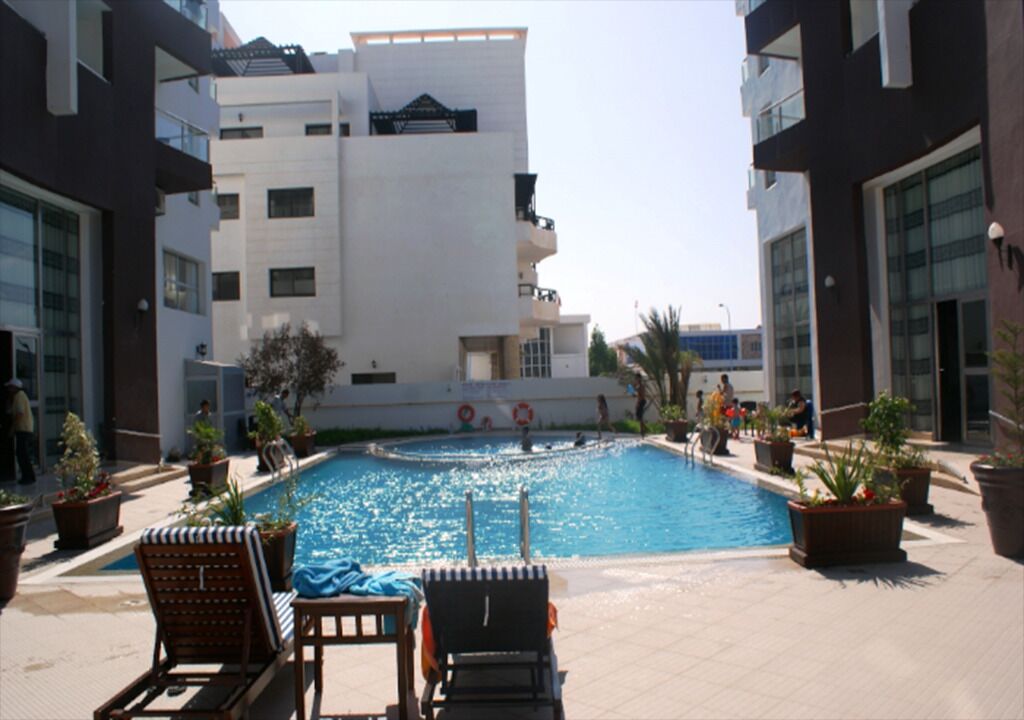 Una piscina con lettini da sole e piante in vaso, circondata da edifici moderni.