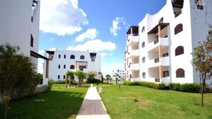 Un camino conduce a un edificio blanco con varios balcones y un cielo despejado.