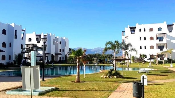 Un resort con edificios blancos, piscina y palmeras.