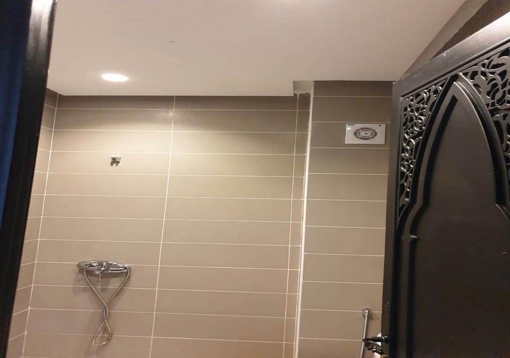 Ein Badezimmer mit beigen Fliesen, einer Duschbrause und einer Ziertür.
