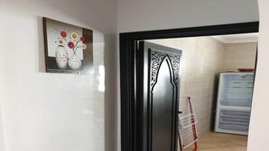 A room with a black-framed door, a tiled wall, and a kitchen area with a refrigerator and a drying rack. - Residence Lilac's Garden 5160 (Cabo Negro)