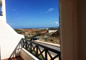 A balcony with a view of a coastal landscape, including a road and distant buildings.