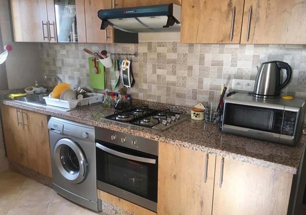 A kitchen with wooden cabinets, a stainless steel washing machine, an oven, a microwave, and a gas stove.