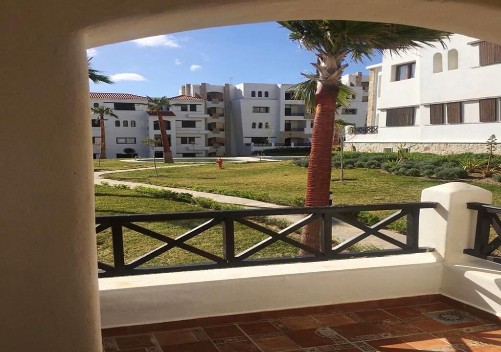En balkon med udsigt over en gårdsplads, palmer og en bygning med flere balkoner.