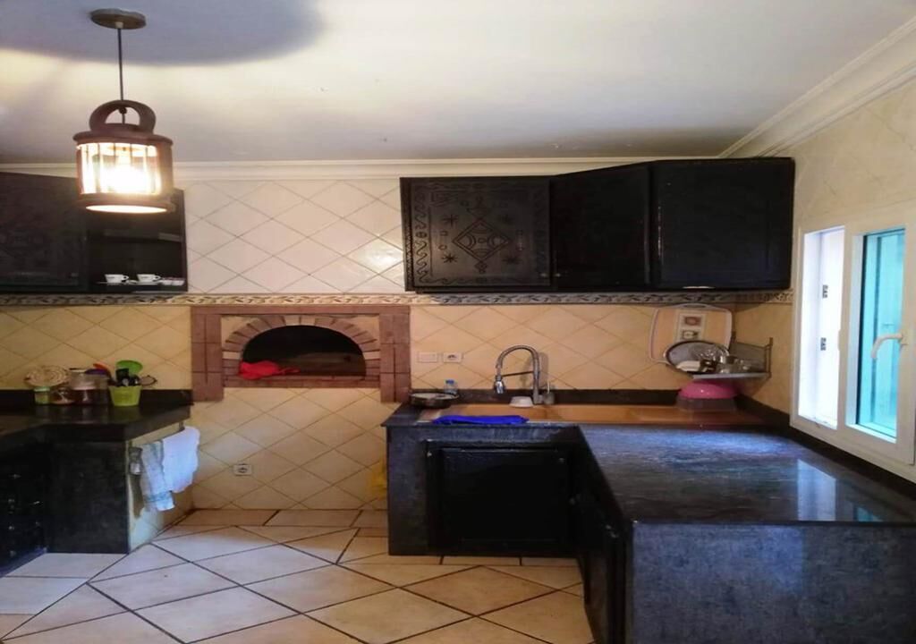 Une cuisine équipée d’un four encastré, d’un évier et d’un luminaire suspendu.