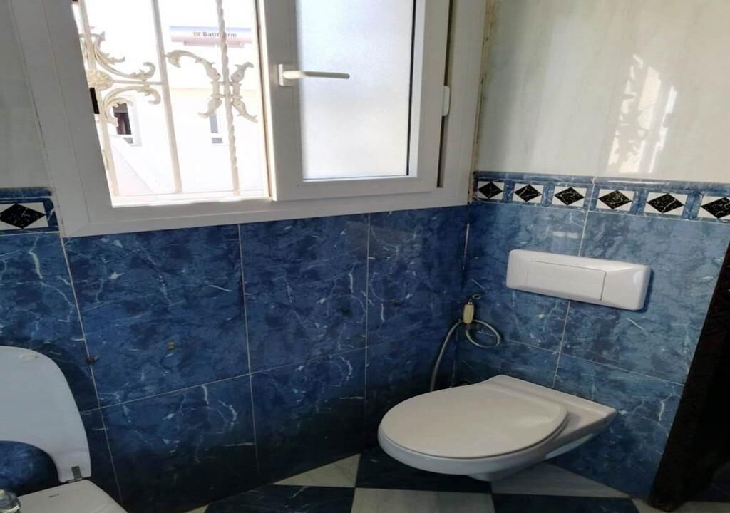A bathroom with a toilet, a bidet, and a window with decorative bars.