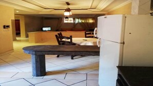 Un comedor con una mesa de piedra, sillas, un refrigerador blanco y un televisor al fondo.