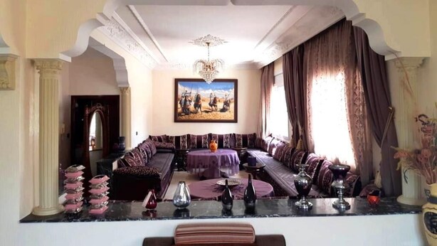 A spacious living room with a large sofa set, a chandelier, and a painting on the wall. - Large Beachfront Villa in Sonaba Agadir 5164 (Agadir)