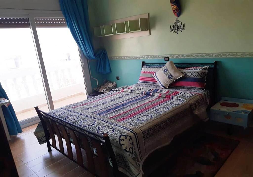 Een slaapkamer met een bed, nachtkastje, dressoir en een raam met gordijnen.