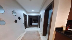 A hallway with a beige rug, geometric wall mirrors, and a door leading to a bedroom. - Residence Hivernage Founty 5165 (Agadir)