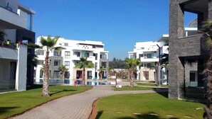 A modern residential complex with multiple-story buildings, a paved walkway, and palm trees. - Residence Hivernage Founty 5165 (Agadir)