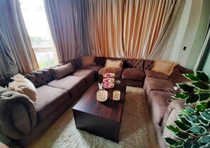 Un salón con un sofá modular, una mesa de centro y un ventanal con cortinas.