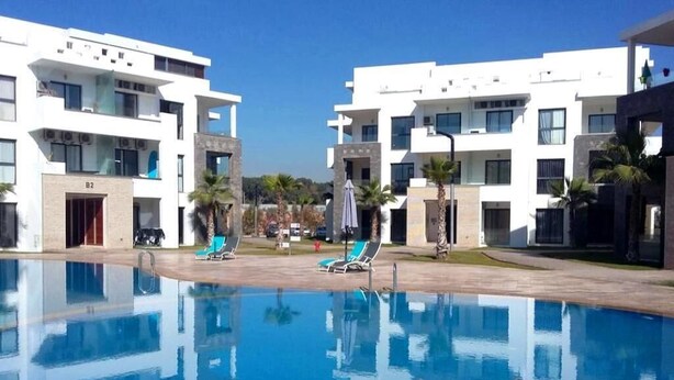 A swimming pool with lounge chairs, a clear sky, and modern buildings in the background. - Residence Hivernage Founty 5165 (Agadir)