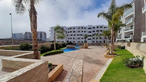 Un pati d'hotel modern amb piscina, palmeres i un jardí ben cuidat.