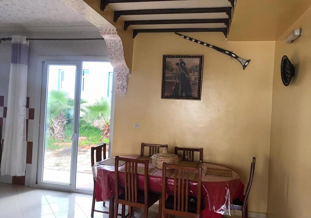 Un coin repas avec une table et des chaises, un tableau accroché au mur et une vue à travers la porte vitrée.
