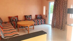 A living room with a sofa set, a round wooden table, and patterned cushions. - Complex Kasbah Lagzira 5203 (Sidi Ifni)