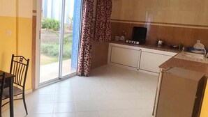 A kitchen with a sliding glass door leading to a patio, a dining table with chairs, and a small refrigerator. - Complex Kasbah Lagzira 5203 (Sidi Ifni)