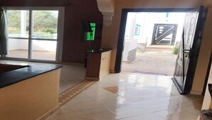 A reception area with a counter, a green screen, and a door leading outside. - Complex Kasbah Lagzira 5203 (Sidi Ifni)