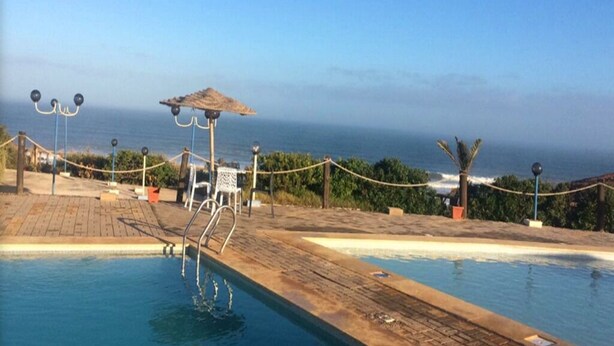 Zona de piscina con terraza de madera, un espacio cubierto para sentarse y vista al océano.