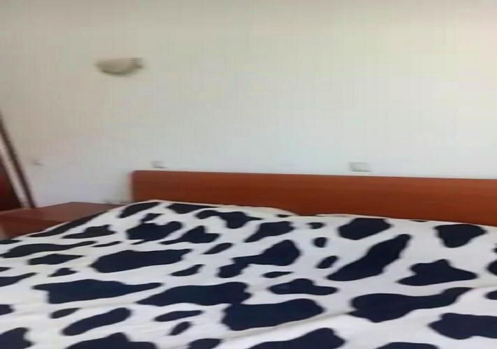 Una cama con una colcha de diseño blanco y negro, un cabecero de madera y una pared blanca con interruptor de luz.