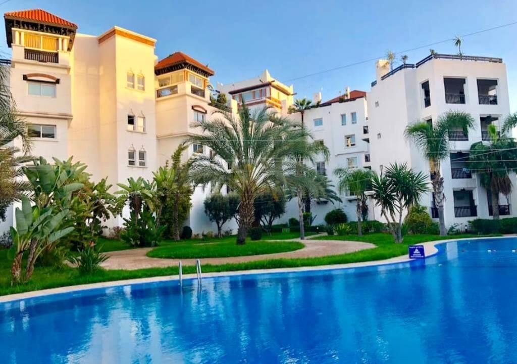 Une piscine entourée d’une végétation luxuriante et de bâtiments blancs dotés de balcons.