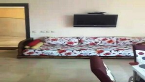 Ein Wohnzimmer mit einer Couch, einem an der Wand montierten Fernseher und einer Holztür.
