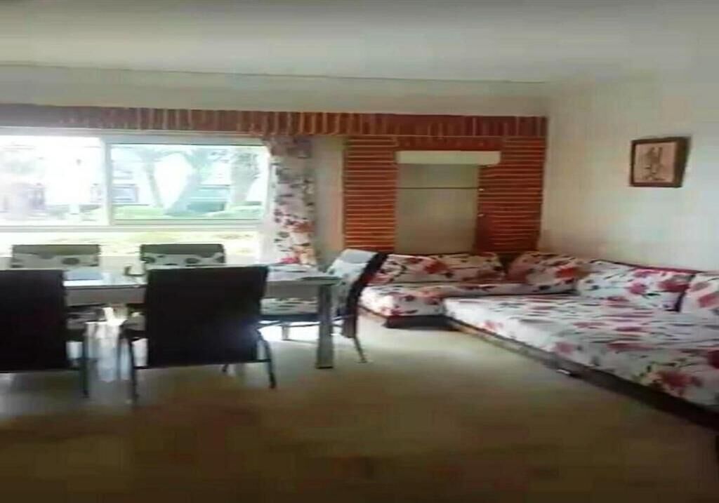En stue med sofa, spisebord med stole og et vindue med persienner.