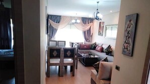 Una sala de estar con un sofá, una mesa de comedor con sillas y una araña.