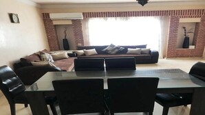 A living room with a glass-top dining table, black chairs, a sofa, and a brick accent wall. - Residence Marina Agadir 5218 (Agadir)