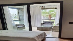 A bedroom with a bed, a sliding glass door leading to an outdoor seating area with a table and chairs, and a view of a pool and palm trees. - Residence Hivernage Founty 5227 (Agadir)