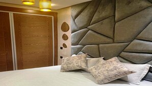 Une chambre à coucher au design moderne, avec un grand lit agrémenté d’oreillers à motifs, une tête de lit géométrique et une armoire en bois.