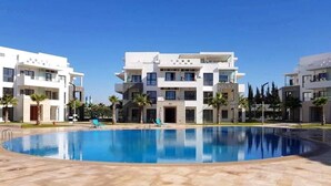 Un immeuble d’appartements moderne doté d’une piscine centrale, de nombreux balcons et offrant une vue sur un ciel d’un bleu éclatant.