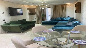 Un salon moderne avec une table basse en verre, des canapés verts et bleus, et un téléviseur à écran plat fixé au mur.