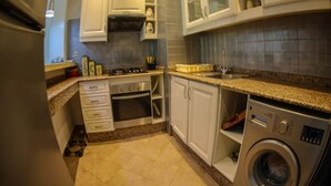 A compact kitchen with white cabinets, a built-in oven, a washing machine, and a granite countertop.