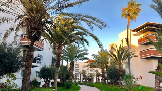 A pathway leading through a garden with palm trees and a building with balconies.