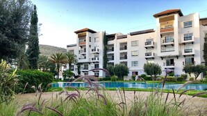 A multi-story hotel with balconies, a swimming pool, and lush greenery.