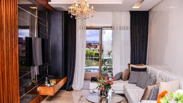 A modern living room with a sofa, coffee table, and a TV. There is a view of the outdoors through large windows. - Residence Marrakech Prestigia Golf City 5244 (Marrakech)