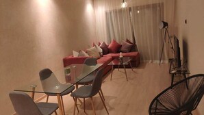 A modern living room with a glass dining table, red sofa with cushions, and a black chair. - Residence Marrakech Prestigia Golf City 5246 (Marrakech)