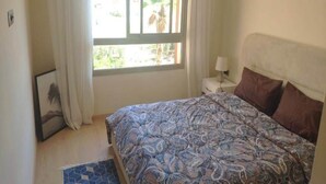 A bedroom with a bed, a nightstand, a lamp, and a window with curtains. - Residence Marrakech Prestigia Golf City 5246 (Marrakech)