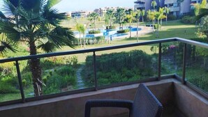 A balcony with wicker furniture, a view of a landscaped area with palm trees and a pool. - Residence Marrakech Prestigia Golf City 5246 (Marrakech)