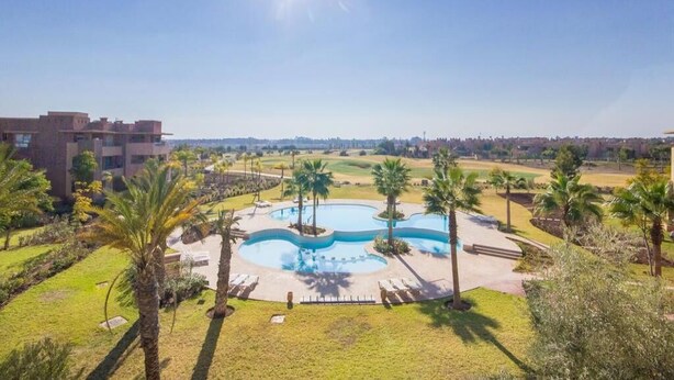 A pool area with palm trees and a building in the background. - Residence Marrakech Prestigia Golf City 5246 (Marrakech)