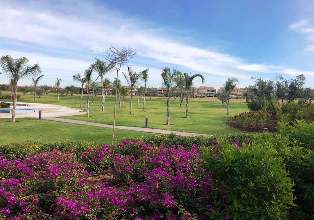 Un parcours de golf avec une pelouse bien entretenue, des palmiers et des fleurs violettes au premier plan.