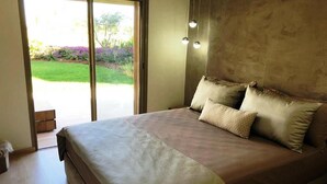 A bedroom with a large bed, a sliding glass door to a garden, and a wall-mounted light fixture. - Residence Marrakech Prestigia Golf City 5280 (Marrakech)