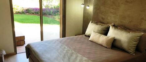 A bedroom with a large bed, a sliding glass door to a garden, and a wall-mounted light fixture.