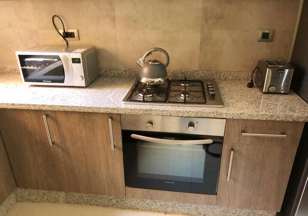 A kitchen with a microwave, kettle, toaster, oven, and granite countertop.