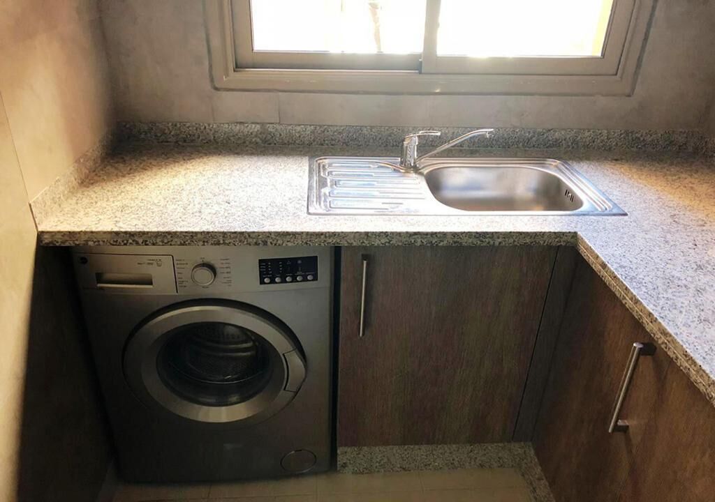 Una cucina compatta con lavatrice e asciugatrice integrate, lavello e finestra che permette l'ingresso di luce naturale.