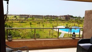 Ein Balkon mit Blick auf ein Schwimmbad, Grünflächen und Gebäude in der Ferne.