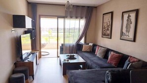 Ein modernes Wohnzimmer mit einer Couch, einem Couchtisch und einem Fernseher. Eine Schiebetür aus Glas führt zu einem Balkon.