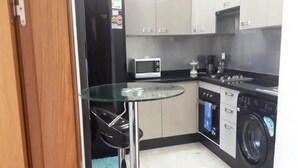 Een compacte keuken met een glazen tafel, een magnetron, een koffiezetapparaat en een wasmachine.