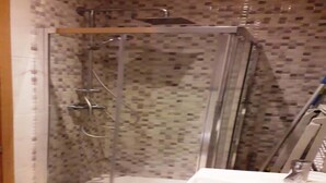 Een douche met glazen wanden, een betegelde muur, een wit wastafelmeubel en een kraan.
